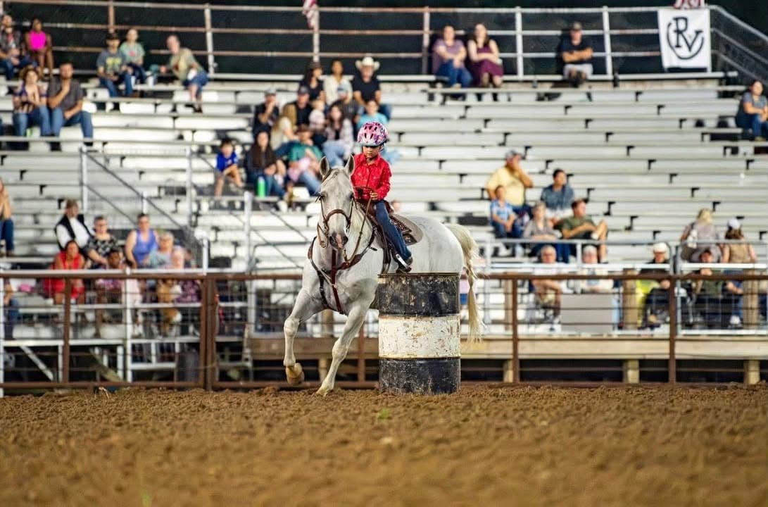 A rider turning her grey horse tight around the barrel in front of a full grandstand