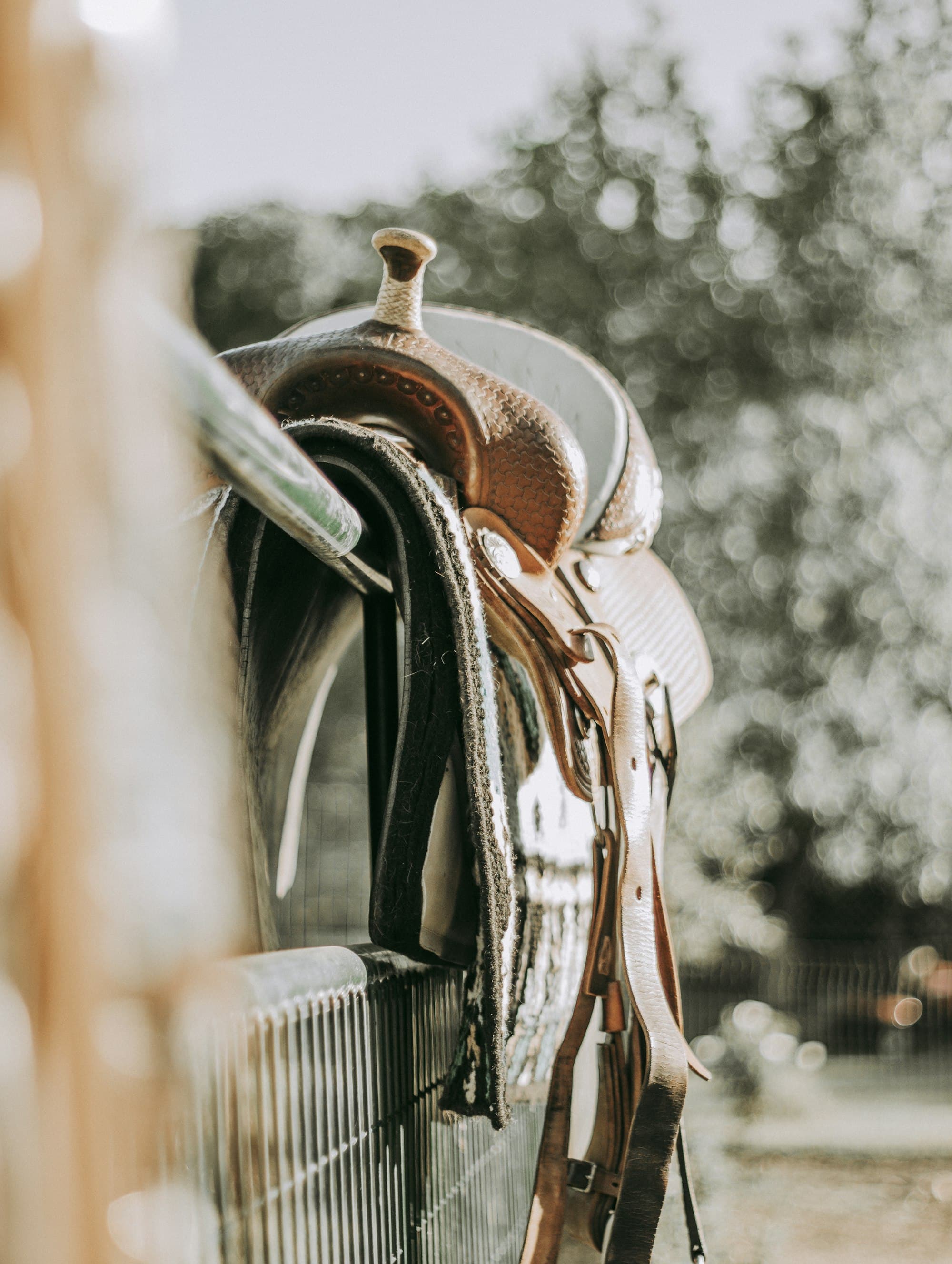 A tooled western saddle and blanket resting over an arena rail